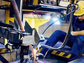 Worker wearing protective clothing and helmet operating a large industrial machine in a manufacturing facility